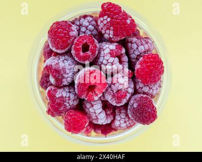 framboises congelées dans un plat en verre vue de dessus, fond jaune Banque D'Images