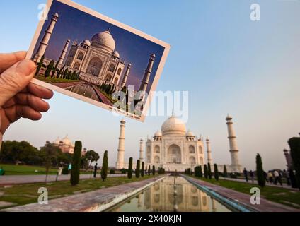 Main d'homme tenant une photo de carte postale du Taj Mahal avec le vrai Taj Mahal derrière ; Agra, Inde Banque D'Images