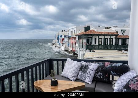 Confortable, balcon au bord de l'eau avec vue sur le ciel gris orageux et les bâtiments blanchis à la chaux le long de la rive de la mer Égée sur l'île de la mer Égée du Sud... Banque D'Images
