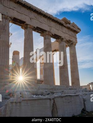 Vue rapprochée des colonnes du Parthénon contre un ciel bleu et nuageux avec un éclat de soleil au crépuscule sur l'Acropole d'Athènes, une ancienne citadelle... Banque D'Images