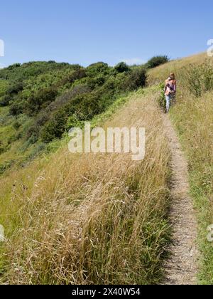 Vue prise de derrière d'une femme marchant le long d'un sentier herbeux sur un sentier côtier dans le sud de l'Angleterre près de Beachy Head Banque D'Images