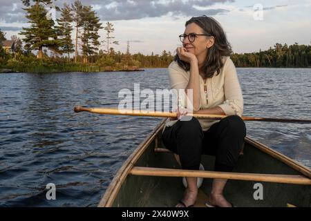 Femme se détend dans un canot flottant comme elle regarde la beauté naturelle le long de la rive du lac ; Lac des bois, Ontario, Canada Banque D'Images