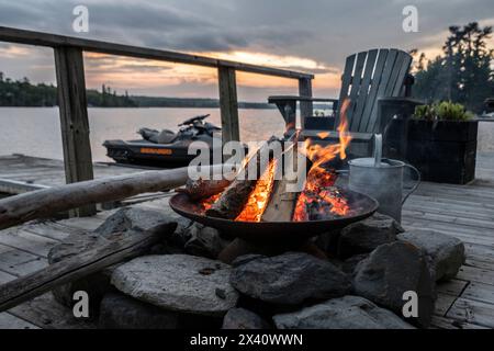 Feu brûlant dans un foyer sur un quai au crépuscule ; Lac des bois, Ontario, Canada Banque D'Images