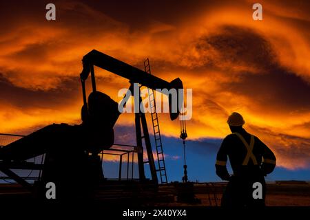 Silhouette d'ouvrier masculin et de citrouille contre un ciel coloré et spectaculaire couché de soleil avec des nuages chauds et incandescents, à l'ouest d'Airdrie ; Alberta, Canada Banque D'Images