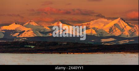 Chaîne de montagnes enneigée éclatante avec la lumière chaude du lever du soleil et les nuages chauds et incandescents avec les contreforts et le champ enneigé au premier plan,... Banque D'Images