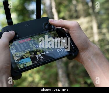 Mains tenant une télécommande de drone avec écran montrant la vue aérienne du drone de la cime des arbres et des bâtiments ; Lac des bois, Ontario, Canada Banque D'Images