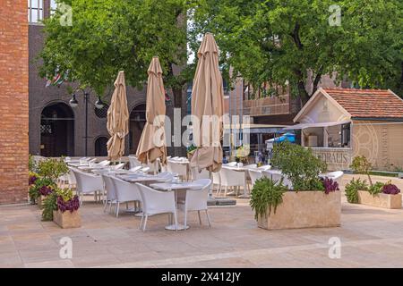 Szeged, Hongrie - 30 juillet 2022 : chaises et tables Restaurant terrasse devant la cathédrale. Banque D'Images