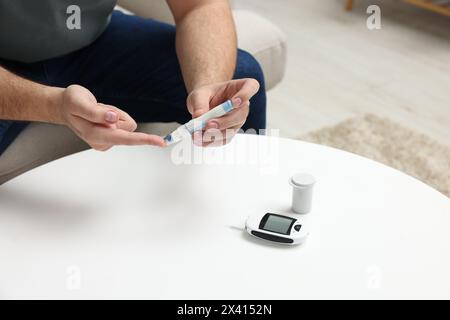 Le test du diabète. Homme vérifiant le taux de sucre dans le sang avec un stylo lancette à la table blanche, gros plan Banque D'Images