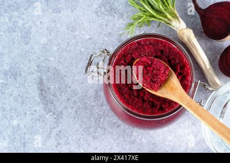 Sauce crémeuse au raifort de betterave en pot avec une cuillère en bois sur le dessus sur un fond gris. Apéritif ou condiment pour viande et poisson. Nourriture végétalienne saine. à Banque D'Images