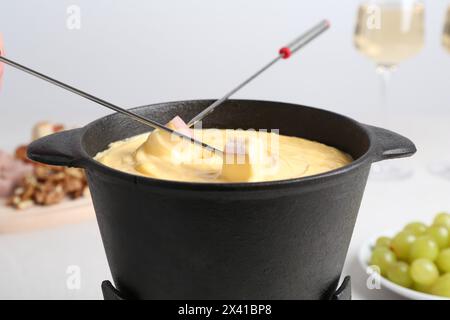 Tremper le jambon dans un pot à fondue avec du fromage fondu savoureux à table, gros plan Banque D'Images