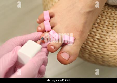 Pédicuriste professionnel peignant les ongles des orteils du client avec du vernis dans le salon de beauté, gros plan Banque D'Images