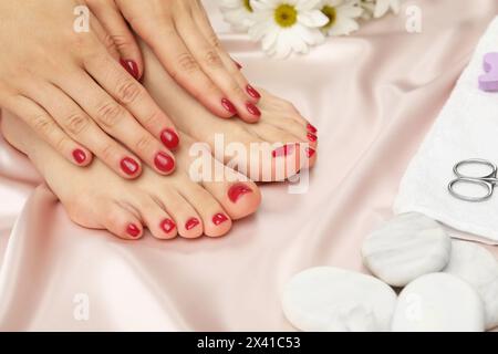 Femme montrant des ongles d'orteils élégants après une procédure de pédicure et des mains manucurées avec un vernis rouge sur un tissu de soie léger, gros plan Banque D'Images