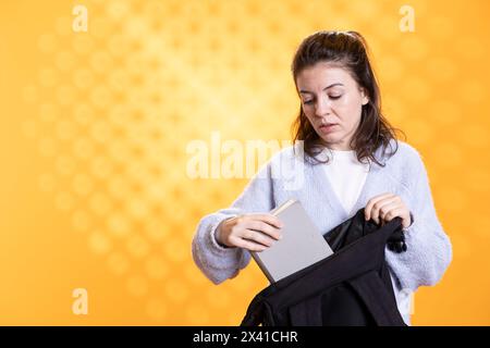 Portrait de femme fouillant à travers le sac à dos, prenant le livre, isolé sur fond de studio. Élève enlevant le manuel utilisé à des fins éducatives du sac à dos de l'école Banque D'Images