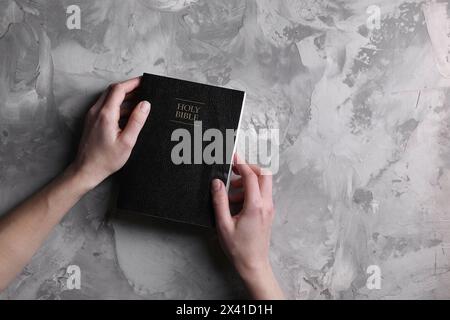 Religion. Femme chrétienne priant sur la Bible à la table texturée grise, vue de dessus. Espace pour le texte Banque D'Images