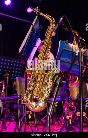 Un saxophone est sur un stand à côté d'un stand de musique. Le saxophone est une couleur or brillant Banque D'Images