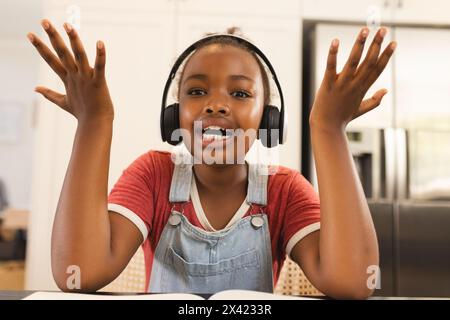 Fille afro-américaine avec des écouteurs, levant les mains excitées à la maison Banque D'Images