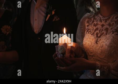 les mains de la mariée et du marié tiennent une bougie allumée le jour du mariage pendant la cérémonie Banque D'Images