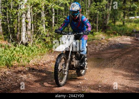 RÉPUBLIQUE DE CARÉLIE, RUSSIE - VERS JUIN 2022 : tournoi hors route Ladoga Trophy 2022 en Carélie. Une fille de coureur de moto sur une moto de sport enduro roule le long d'une route forestière dans une course Banque D'Images