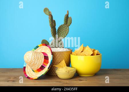 Chapeau sombrero mexicain, cactus, croustilles de nachos et guacamole dans des bols sur une table en bois sur fond bleu clair Banque D'Images