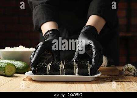 Chef en gants faisant des rouleaux de sushi à la table en bois, gros plan Banque D'Images