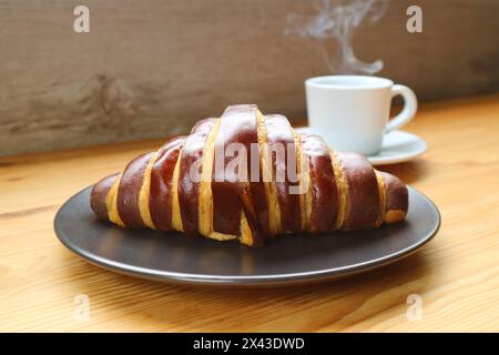 Délicieux croissant au chocolat avec une tasse de café aromatique fumant en toile de fond Banque D'Images