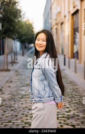 Portrait d'une jeune belle femme asiatique souriante debout sur le trottoir d'une rue de la ville. Banque D'Images