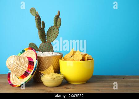 Chapeau sombrero mexicain, cactus, puces de nachos et guacamole dans des bols sur une table en bois sur fond bleu clair, espace pour le texte Banque D'Images