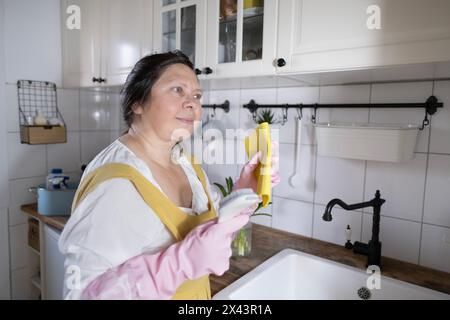 femme mature pleine figure nettoyant la cuisine en gants de ménage en caoutchouc rose, protection des mains, reflétant les thèmes des émotions, de la maison et de la relaxation, divis Banque D'Images