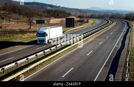 Gros camion blanc avec une remorque blanche sur une route de campagne en mouvement contre un ciel nocturne Banque D'Images