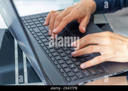 Gros plan de la femme avec de belles mains dans la tenue d'affaires, travaillant sur l'ordinateur portable dans le bureau Banque D'Images