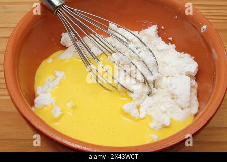 Préparation de cheesecake avec oeuf et fromage cottage dans un pot en argile avec fouet. Banque D'Images