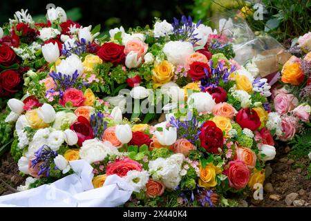 une couronne funéraire avec un ruban blanc et de nombreuses fleurs colorées sur une tombe après des funérailles Banque D'Images