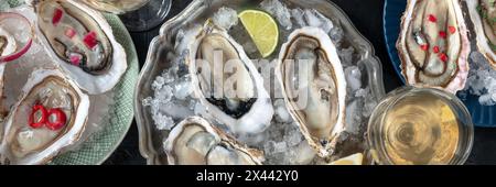 Huîtres sur glace panorama, avec diverses garnitures et vin blanc, plan de pose à plat au-dessus sur un fond de pierre noire Banque D'Images