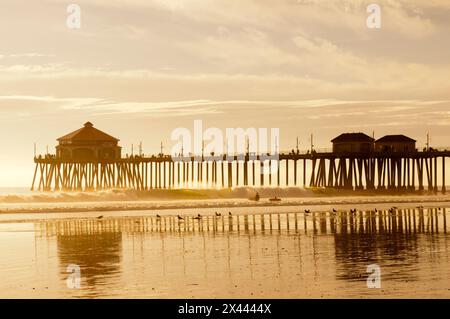 La jetée de Huntington Beach et les surfeurs au coucher du soleil.Huntington Beach, Californie. Banque D'Images