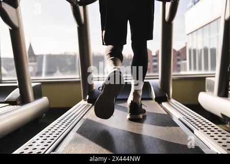 Un homme sportif en vêtements d'activité marche énergiquement sur un tapis roulant à la salle de gym, se concentrant sur sa routine d'entraînement. Banque D'Images