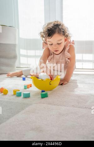 belle petite fille aux cheveux bouclés joue concentré avec jeu d'équilibrage de blocs et de pièces en bois colorées. montessori material development, cr Banque D'Images