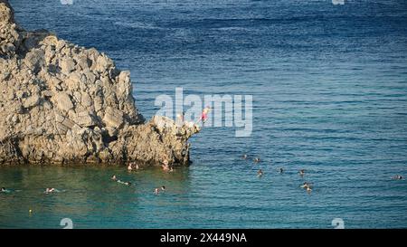 Les gens sautant des falaises dans la mer, entourés de nageurs dans l'eau claire, Lindos, Rhodes, Dodécanèse, îles grecques, Grèce Banque D'Images