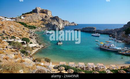 Journée de plage ensoleillée avec vue sur une baie, des falaises et des bateaux garés, Paulus Bay, en contrebas de l'Acropole de Lindos, Lindos, Rhodes, Dodécanèse, îles grecques Banque D'Images