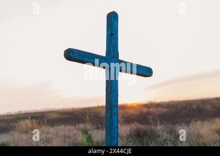 Croix en bois bleue debout au milieu de hautes herbes au coucher du soleil Banque D'Images