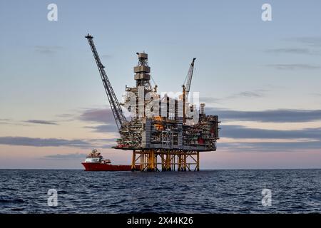 Plate-forme offshore de jackup de pétrole et de gaz, pendant les opérations de fret avec navire de ravitaillement dans la mer et beau ciel coloré de coucher de soleil. Banque D'Images