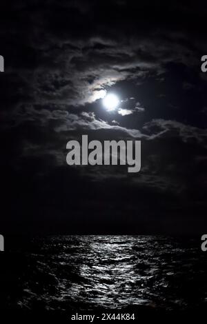 La pleine lune brille à travers les nuages la nuit dans la mer. Banque D'Images