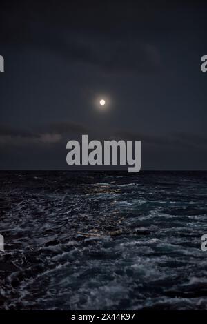 Pleine lune dans le ciel au-dessus de la mer la nuit par temps orageux Banque D'Images