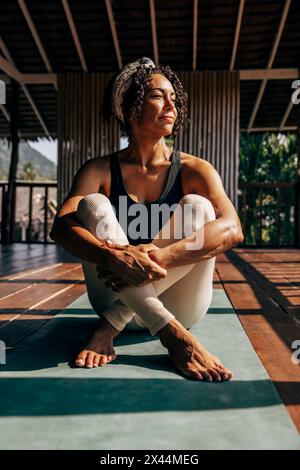 Femme mature serrant les genoux tout en étant assise sur le tapis de yoga au centre de bien-être Banque D'Images