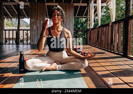 Femme mature tenant des cloches tibétaines et méditant tout en étant assise sur un tapis de yoga au centre de bien-être Banque D'Images