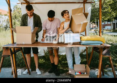 Groupe de volontaires masculins et féminins étiquetant des boîtes sur la table pendant la campagne caritative au centre communautaire Banque D'Images