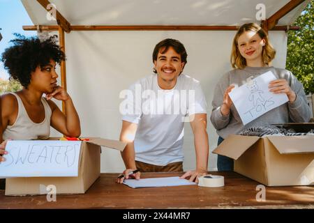 Groupe de bénévoles multiraciaux souriants étiquetant des boîtes avec des étiquettes de nom pendant la campagne caritative au centre communautaire Banque D'Images