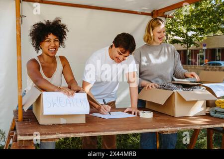 Portrait de bénévoles féminines heureuses étiquetant des boîtes avec des collègues tout en travaillant pendant la campagne caritative au centre communautaire Banque D'Images