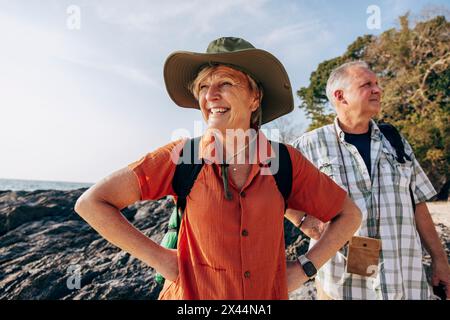 Femme heureuse avec les mains sur la hanche debout à côté de l'homme à la plage en vacances Banque D'Images