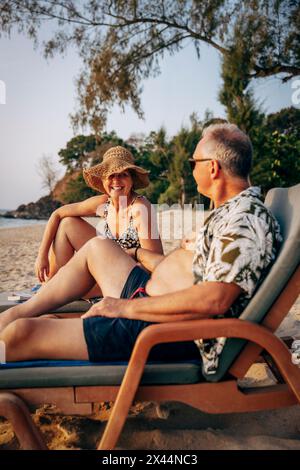 Heureux couple senior s'amusant tout en étant assis sur une chaise longue à la plage Banque D'Images