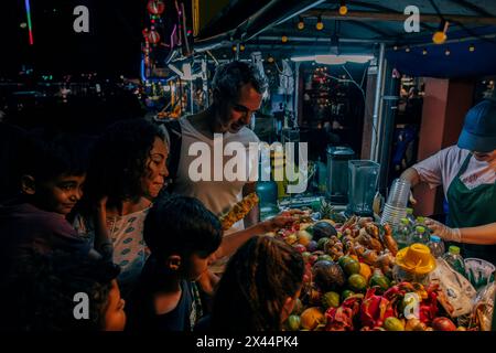 Famille achetant du jus de fruits à l'étal de fruits au marché alimentaire en vacances Banque D'Images